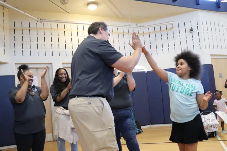 Sean Auton, an HMB attorney, gives a young girl a high five in a gymnasium.